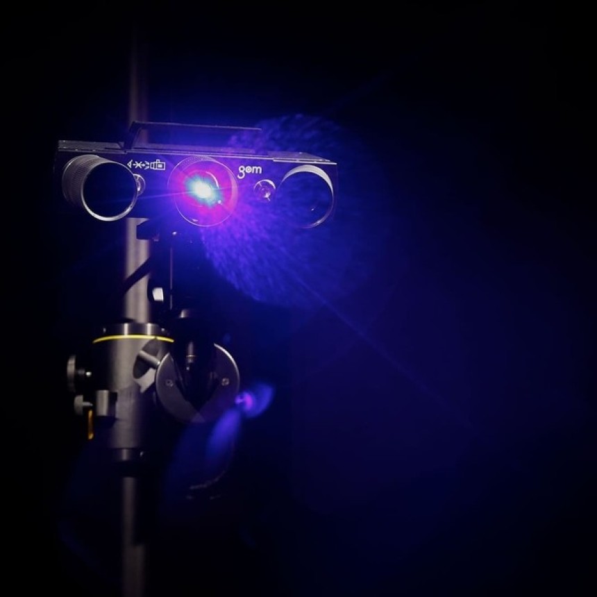 High-precision 3D scanner with blue laser light mounted on a tripod in a dark environment for dimensional inspection.