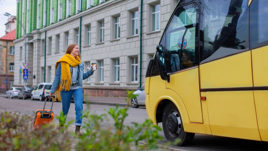 A mini bus is parked outside on the road, and a girl is coming towards it
