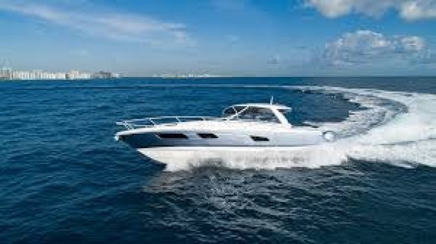 Luxury white motor yacht cruising at high speed on clear blue ocean with city skyline in the background.