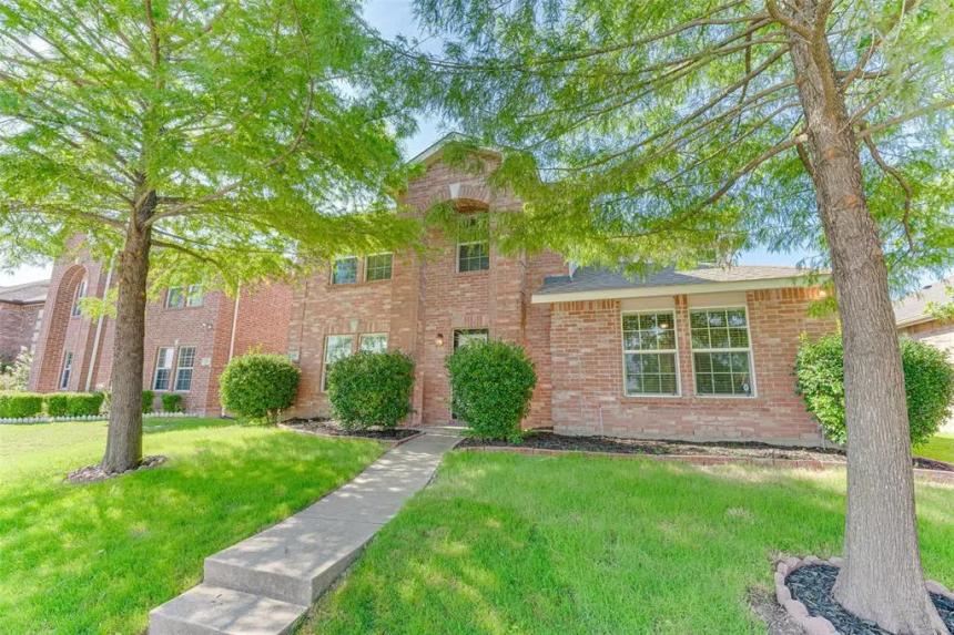 Two-story brick house with front walkway, green lawn, and mature trees in a quiet residential neighborhood.