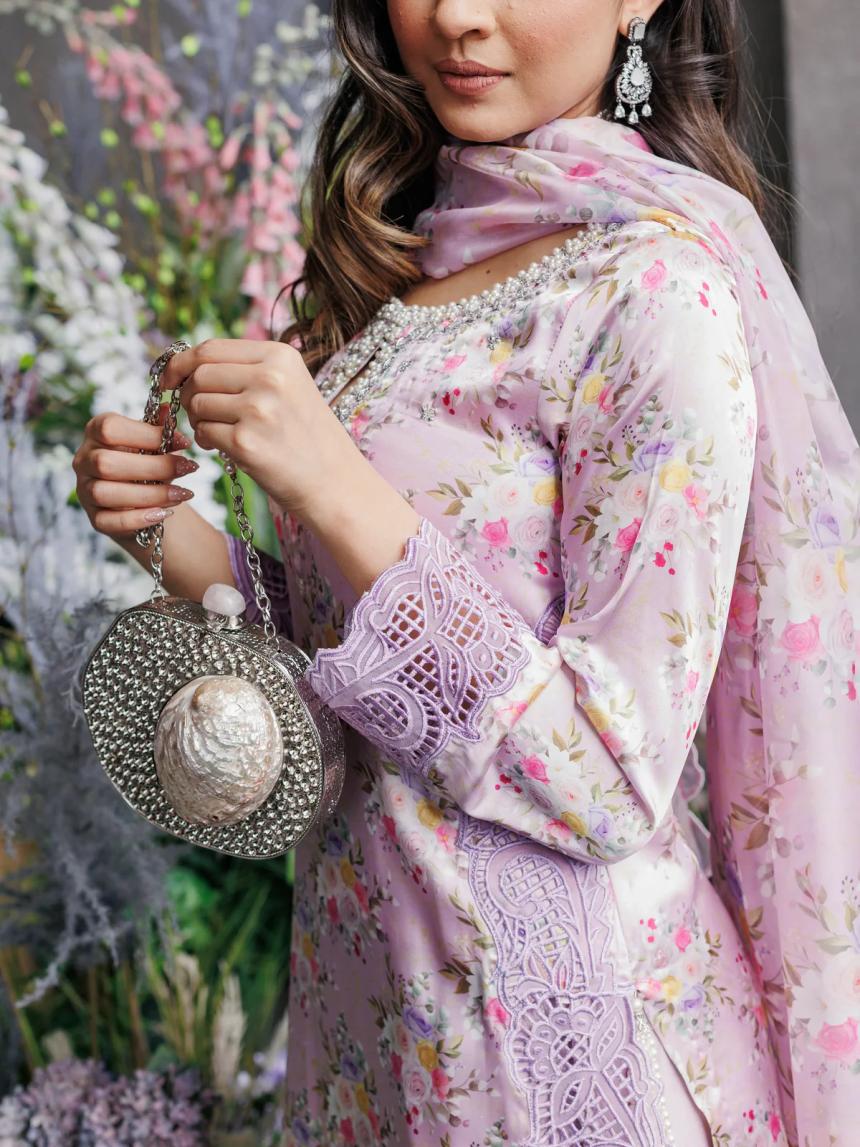 Woman wearing a pastel pink floral embroidered traditional outfit with lace details, statement earrings, and holding a silver embellished clutch bag.